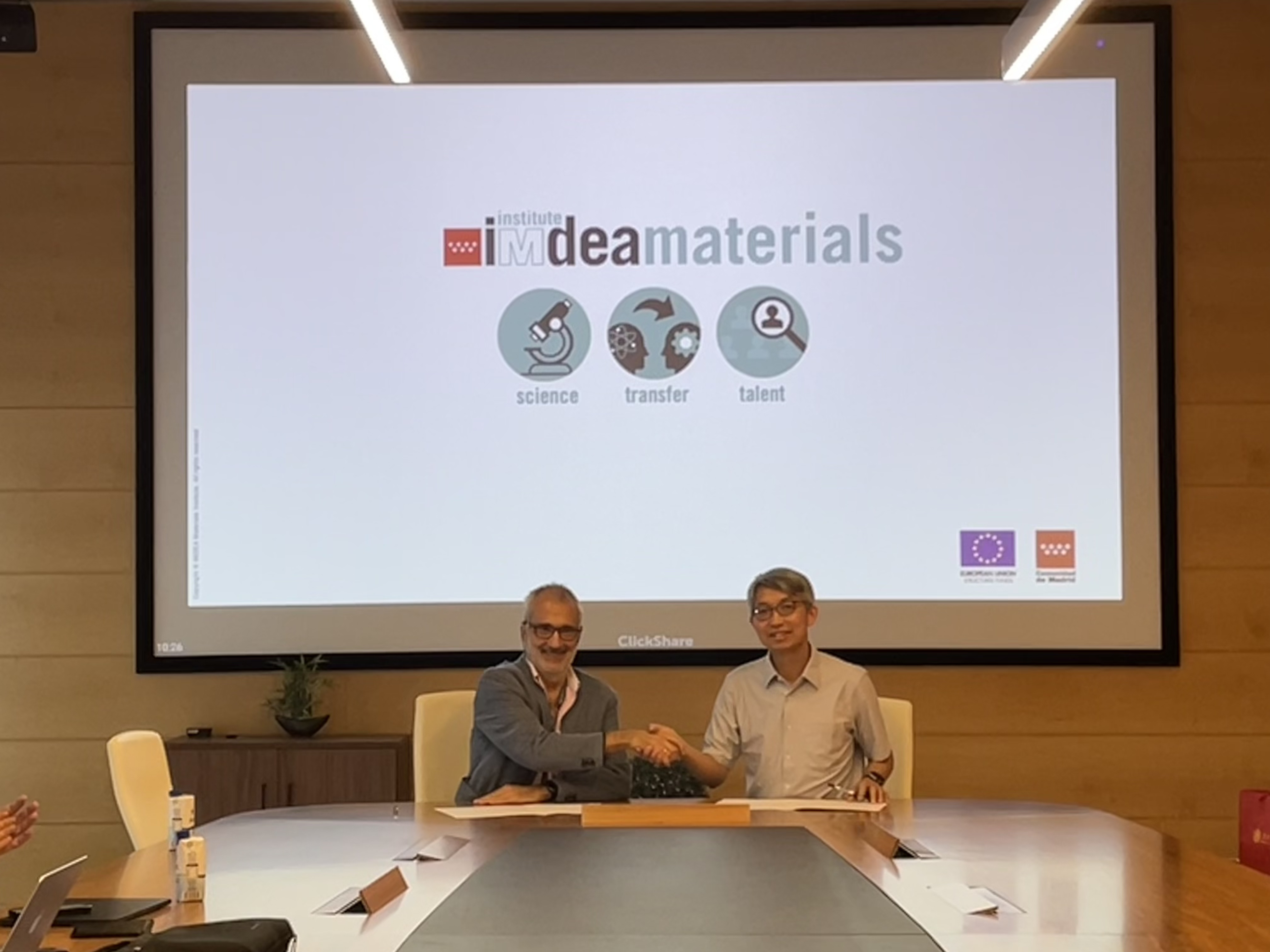 A group of men sitting at a table with a projector screen

Description automatically generated